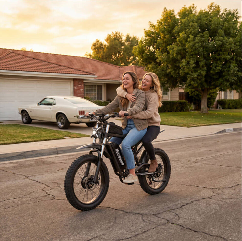 Two women riding a black electric bike on a suburban street with a classic car in the background. Moveloop T1 Ultra Electric Bike for Adults 3000W Peak Motor 48V 20AH 35 MPH 40-80 Miles All Terrain Fat Tire Electric Mountain Bike