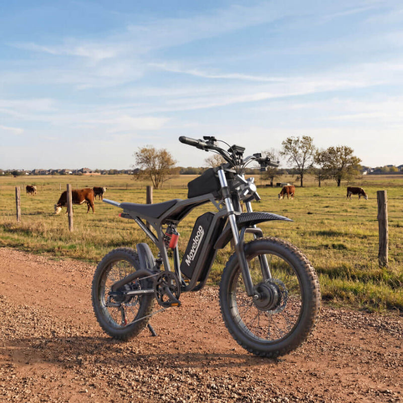 Electric bike on a dirt road with a rural landscape and cows in the background Moveloop T1 Ultra Electric Bike for Adults 3000W Peak Motor 48V 20AH 35 MPH 40-80 Miles All Terrain Fat Tire Electric Mountain Bike